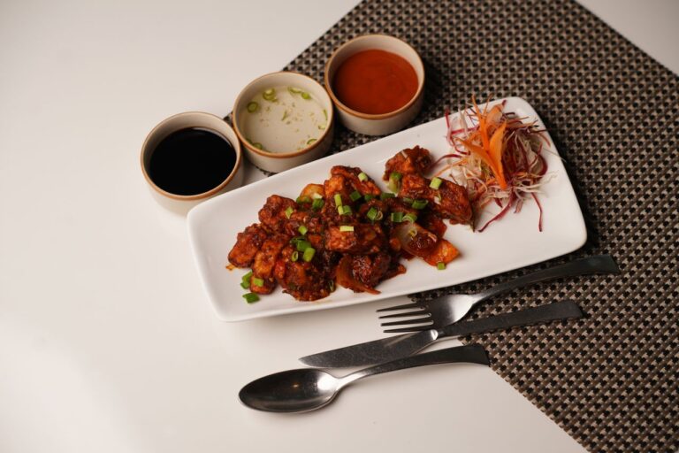 Plate of Asian-style crispy chicken with side sauces and garnished vegetables on a dining table.