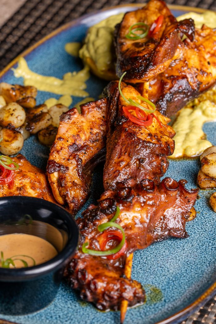 Tasty grilled chicken skewers on a plate with vegetables and dipping sauce.
