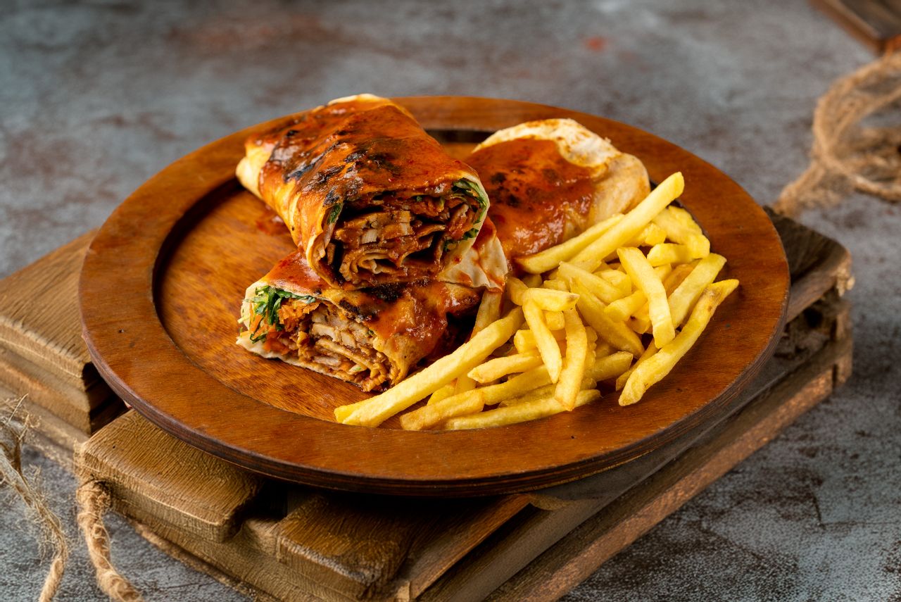 Close-up of chicken shawarma with french fries on a rustic plate.