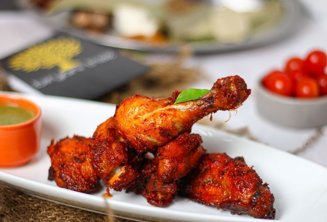 Close-up of spicy tandoori chicken drumsticks served with green chutney, showcasing vibrant Indian cuisine.