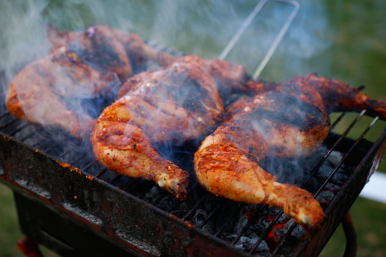 Close-up of spicy chicken grilling on a charcoal barbecue with visible smoke outdoors.